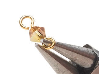 Pliers have completed a single loop in the end of an eye pin, completing a bicone drop